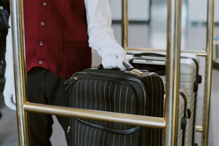 A person in a maroon vest holding a black striped suitcase near a luggage cart. White luggage damage is covered with RestAssure.